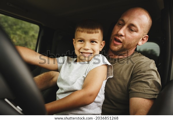 Father teaches\
little son to drive on road\
trip