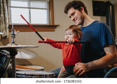 Father Teaching Baby Boy To Play Drums. Parent With Toddler Child Having Fun, Spending Time Together. Dad And Kid Playing Music. Family Hobby Activity And Leisure Time During Self Isolation. 