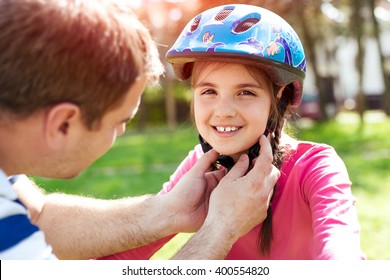 Father Teaching Brave Daughter To Ride Bicycle Putting On Safety Helmet