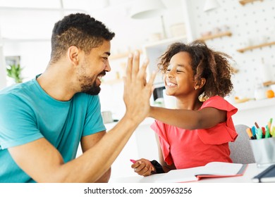 father teaching daughter and helping with homework at home, daughter giving high five to father - Powered by Shutterstock