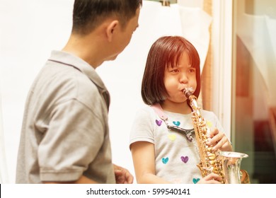 Father Teaching Daughter To Play Saxophone. Dad Train Asian Kid Girl Blow Sax Music Instrument.Asia Teacher With Musical Student Learn Plying Jazz Music. Jazz Appreciation Month In April.