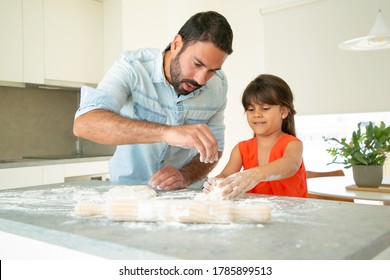 Father Teaching His Girl To Bake Bread Or Pies. Focused Dad And Daughter Kneading Dough On Kitchen Table With Flour Messy. Family Cooking Concept