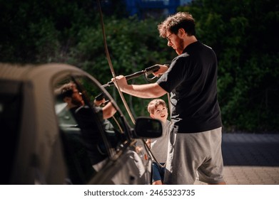 A father teaching his young son to wash a car with a high-pressure hose at a self-service station. The boy looks up at his dad with admiration, sharing a bonding moment - Powered by Shutterstock