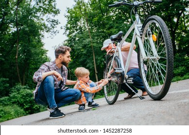 Father Teaching Son Reparing Old Bike Outdoor. Dad, Grandad And School Age Grandson Son Fixing Bicycle At Summer Green Park Outside. Happy Family Relation Different Generation Concept.