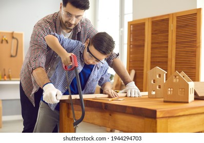 Father teaching son to use sharp handsaw sawing wood plank together at home carpentry workshop. Masculine duties, parent and child common hobby concept. Woodworking, family leisure activity