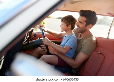 Father Teaching Young Son To Drive Car On Road Trip