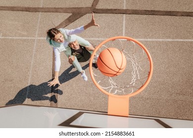 Father and teenage daughter playing basketball outside at court, high angle view above hoop net.