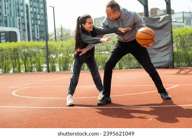 Father and teenage daughter playing basketball outside at court - Powered by Shutterstock