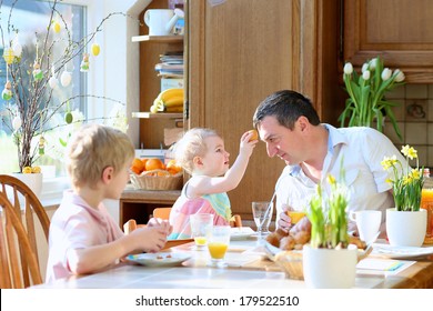 Father With Teenager Son And Toddler Daughter Eating Eggs During Family Breakfast On Easter Day Sitting Together In Sunny Kitchen. Selective Focus On Girl And Man.