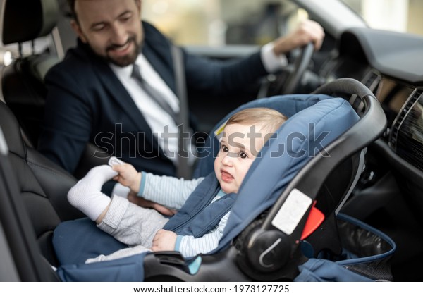 Father tend a child while driving at work with baby
sitting in modern car seat. Child new born traveling safety on the
road. Safe way to travel fastened seat belts in a vehicle with
young kids. 