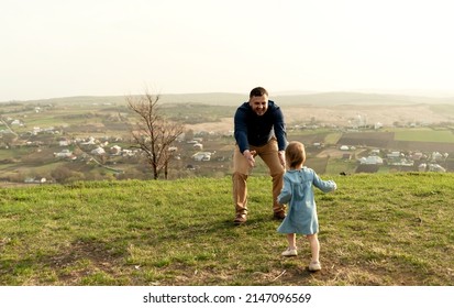 Father Throws Up And Spins His Daughter In Nature In Springtime. Dad And Girl Play In The Park At Sunset. The Girl Is Flying. Friendly Family Concept. Close-up