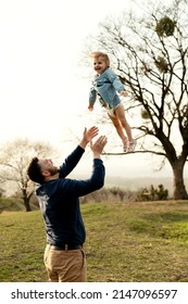 Father Throws Up And Spins His Daughter In Nature In Springtime. Dad And Girl Play In The Park At Sunset. The Girl Is Flying. Friendly Family Concept. Close-up