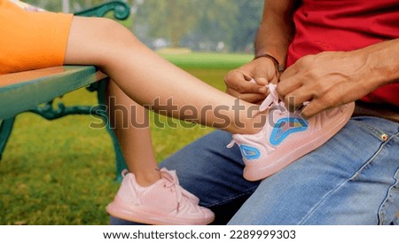 Father ties his daughter's shoes - childcare and parenting. Closeup shot of a caring dad helping his little girl to tie her shoelaces while she is sitting on a bench in the park