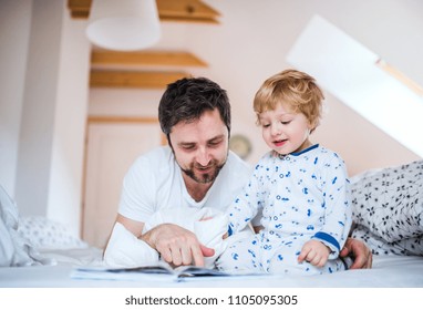 Father With Toddler Boy Reading A Book On Bed At Home At Bedtime.