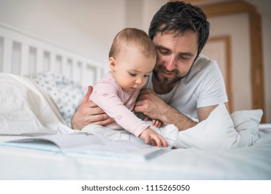 Father With Toddler Girl Reading A Book On Bed At Home At Bedtime.