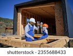 Father with toddler son building wooden frame house. Male builder giving high five to kid on construction site, wearing helmet and blue overalls on sunny day. Carpentry and family concept.