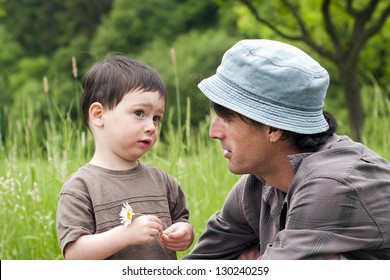 Father With Toddler Son Talking On A Green Summer Meadow.