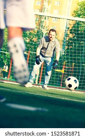 Father Training His Little Son Play In Football. Man With Child Playing Football Outside On Field. Kids Approach Dad In Goal During Family Football Game