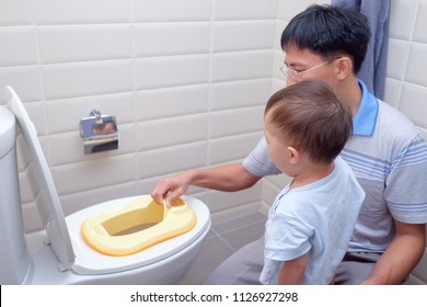 Father Training Sleepy Son To Use Toilet In Bathroom, Cute Little Asian 1 Year Old / 18 Months Toddler Baby Boy Sitting On Toilet With Kid Bathroom Accessory, Potty / Toilet Training Child Concept