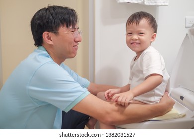 Father Training Smiling Son To Use Toilet In Bathroom, Cute Little Asian 2 Years Old Toddler Baby Boy Sitting On Toilet With Kid Bathroom Accessory, Happy Potty / Toilet Training Concept