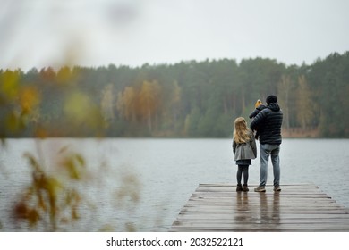 Father And Two Children Having Fun On Late Autumn Day By The Lake. Adorable Baby Boy Being Held By His Daddy. Older Sister Hugging Her Dad And Baby Brother. Family Exploring Nature.