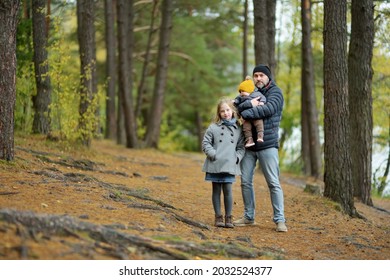 Father And Two Children Having Fun On Late Autumn Day By The Lake. Adorable Baby Boy Being Held By His Daddy. Older Sister Hugging Her Dad And Baby Brother. Family Exploring Nature.