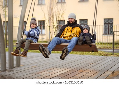 father with two sons sitting on large bench swings together. brothers with dad walking on playground - Powered by Shutterstock