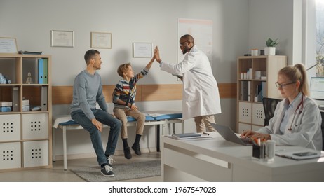 Father Visiting a Friendly Family Doctor with His Young Teenage Son Who Has Broken His Arm, Give High Five. They Talk to an African American Physician in a Hospital Office. Boy is Wearing an Arm Brace - Powered by Shutterstock