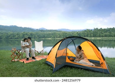 Father watches as his daughter draws on notebook while mother prepares things in a yellow tent, camping with the family - Powered by Shutterstock