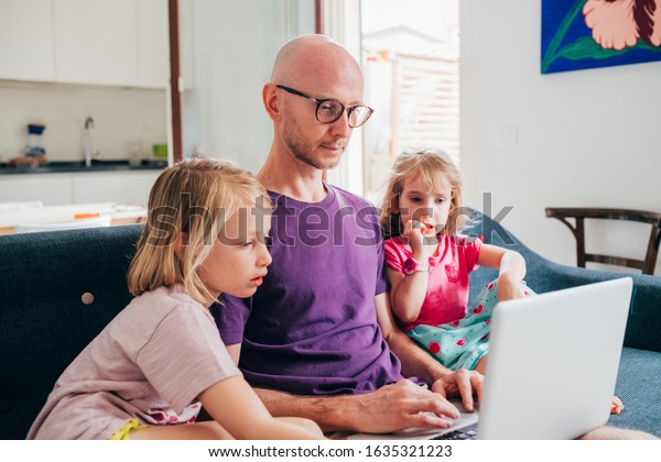 Father watching streaming cartoon on computer\
with two daughters indoor at home - entertainment, technology,\
supervising concept