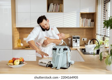 Father In White Shirt Holding Baby In Hands Packing Rucksack For Going Out. Happy Dad Talking By Phone With Wife.