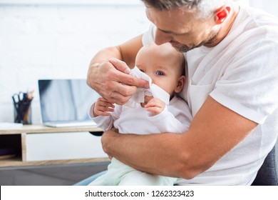 father wiping runny nose of adorable baby daughter with napkin at home