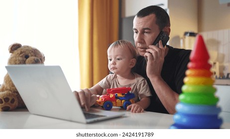 father working from home remotely with baby son in his arms. pandemic remote work business concept. father tries to work at home in kitchen, baby children interfere sitting on their fun hands - Powered by Shutterstock