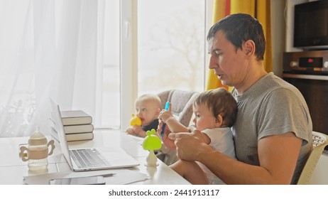 father working from home remotely with baby daughter in his arms. pandemic remote work business concept. father tries to work at home in fun kitchen, baby children interfere sitting on their hands - Powered by Shutterstock