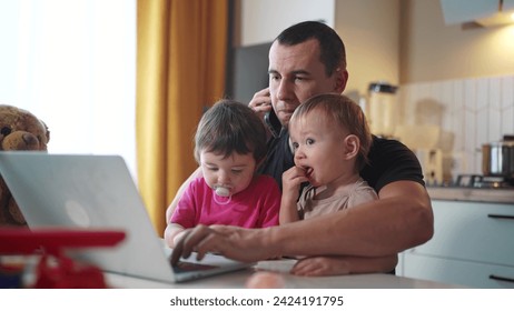 father working from home remotely with two baby in his arms. pandemic remote work business concept. father tries to work at fun home in kitchen, baby children interfere sitting on their hands - Powered by Shutterstock