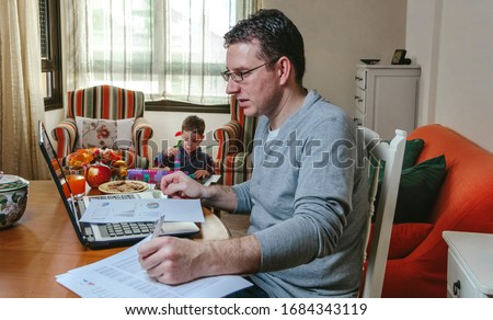 Father working on the laptop in the living room while her son plays
