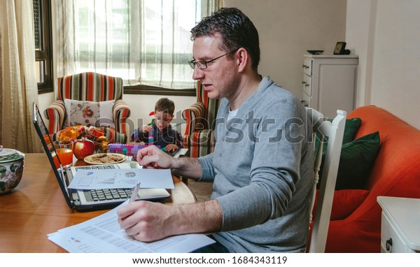 Father working on the laptop in the living room
while her son plays