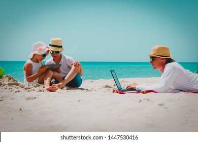 Father Working On Laptop While Kids Looking At Touch Pad At Beach