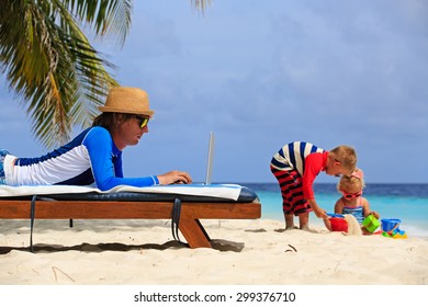 Father Working On Laptop While Kids Play With Sand On Beach