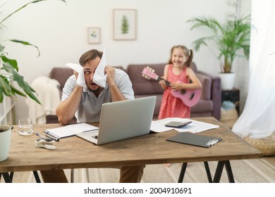 father works at home with a laptop together with his daughter. a little girl wants to play the guitar, make noise. sad man tries to work while working remotely at home - Powered by Shutterstock