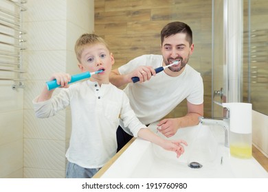 Father And Young Son Brush Their Teeth In The Morning, Have Fun Together