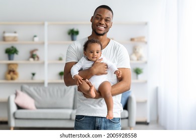 Fatherhood Concept. Portrait Of Happy Young Black Man Holding Cute Newborn Baby In Hands And Looking At Camera, Smiling Millennial Father Bonding With His Infant Child At Home, Copy Space