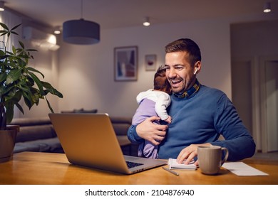 Fatherhood And Remote Business. A Happy Young Father Holding His Little Girl In His Hands And Having An Online Meeting On A Laptop With Colleagues. Super Dad Finishes All Tasks.