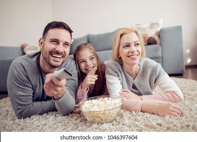 Father,mather and daughter lying on floor ,watching  TV and eating popcorn.