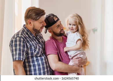 Fathers Admiring Their Growing Daughter. Beautiful Child With Long Blonde Hair. LGBT Parenting Concept.