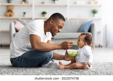 Father's Care. Loving Black Dad Feeding His Cute Baby Son From Spoon At Home, Young African American Daddy Giving Healthy Food To His Little Toddler Child While They Relaxing Together In Living Room - Shutterstock ID 2022074738