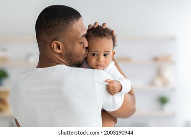 Father's Care. Young Black Dad Holding And Kissing Adorable Newborn Baby At Home, Cute Infant Child Looking At Camera, African American Daddy Bonding With His Son Or Daughter At Home, Closeup Shot