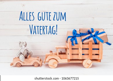 Father's Day card. Wooden car with toy bear and wooden truck with gifts. German greeting "Alles gute zum Vatertag!", which means "Happy Father's Day". - Powered by Shutterstock