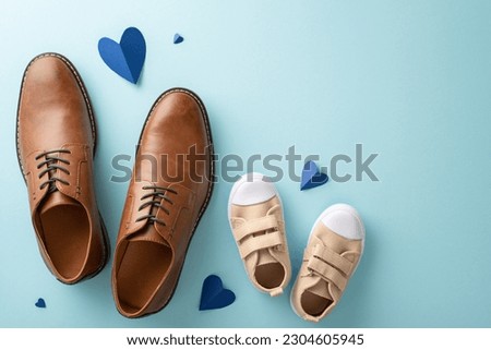 Father's Day celebration with little son. Top view of dad's leather shoes, son's sneakers, and hearts on pastel blue background with empty space