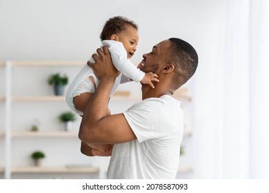 Father's Day Concept. Loving Young Black Dad Lifting Up In Air Cute Infant Baby, Caring African American Daddy Bonding With Adorable Little Child At Home, Enjoying Spending Time Together, Copy Space